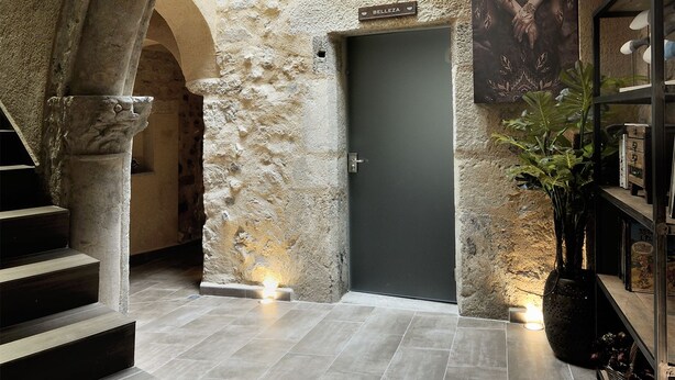 Ein Korridor mit Steinwänden, einer dunklen Tür, einer Treppe und einem Blumentopf.