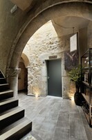 Corredor de paredes de pedra com uma porta escura, escada e um vaso de planta.
