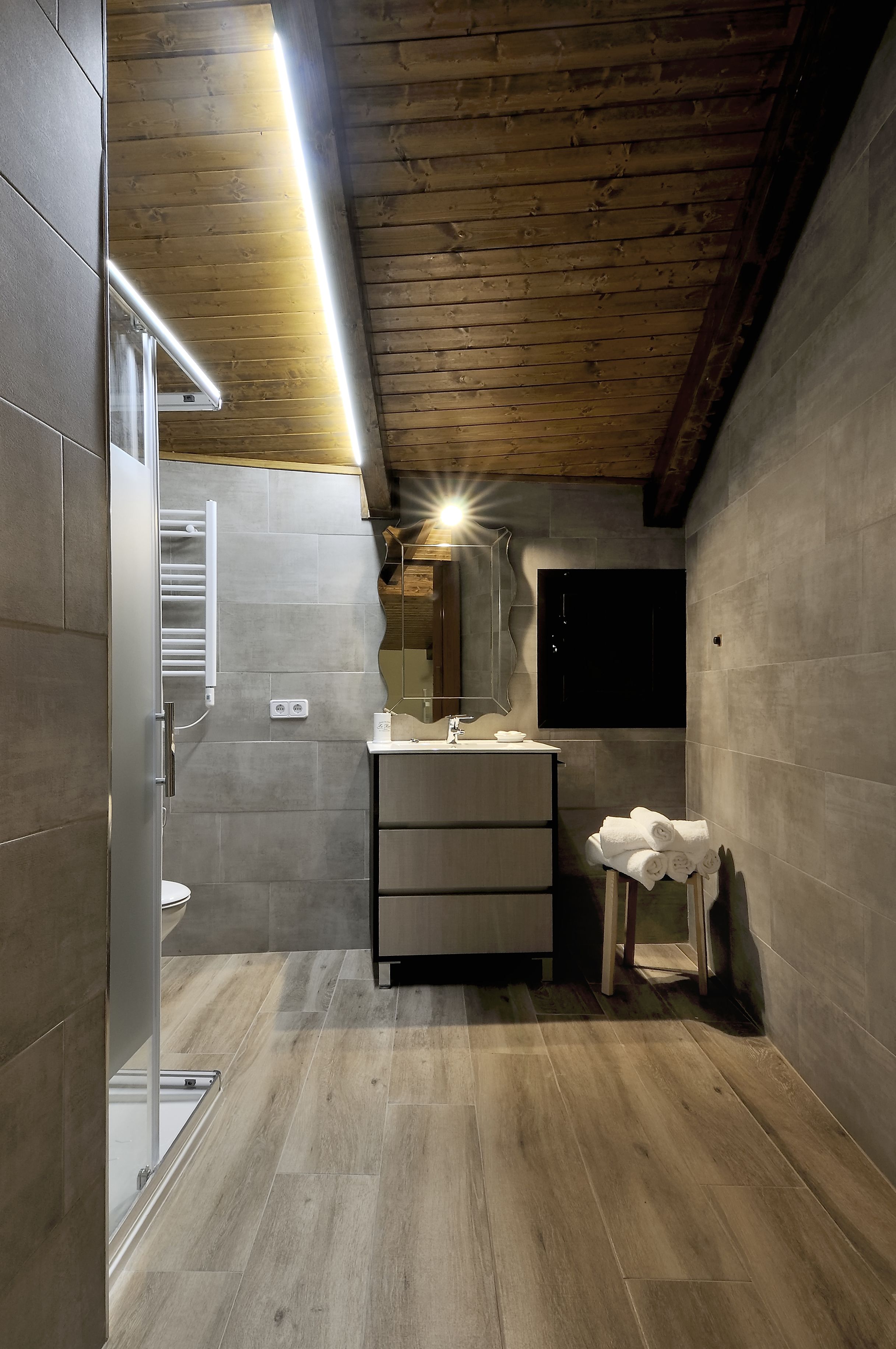Un baño moderno con techo de madera, un espejo grande, un lavamanos y un inodoro.