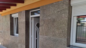 Um edifício com fachada de pedra, pérgola de madeira e janela com moldura branca.