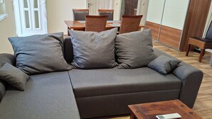Um sofá cinzento com três almofadas, uma mesa de centro de madeira e um espaço de jantar com cadeiras de vime e uma mesa de madeira.