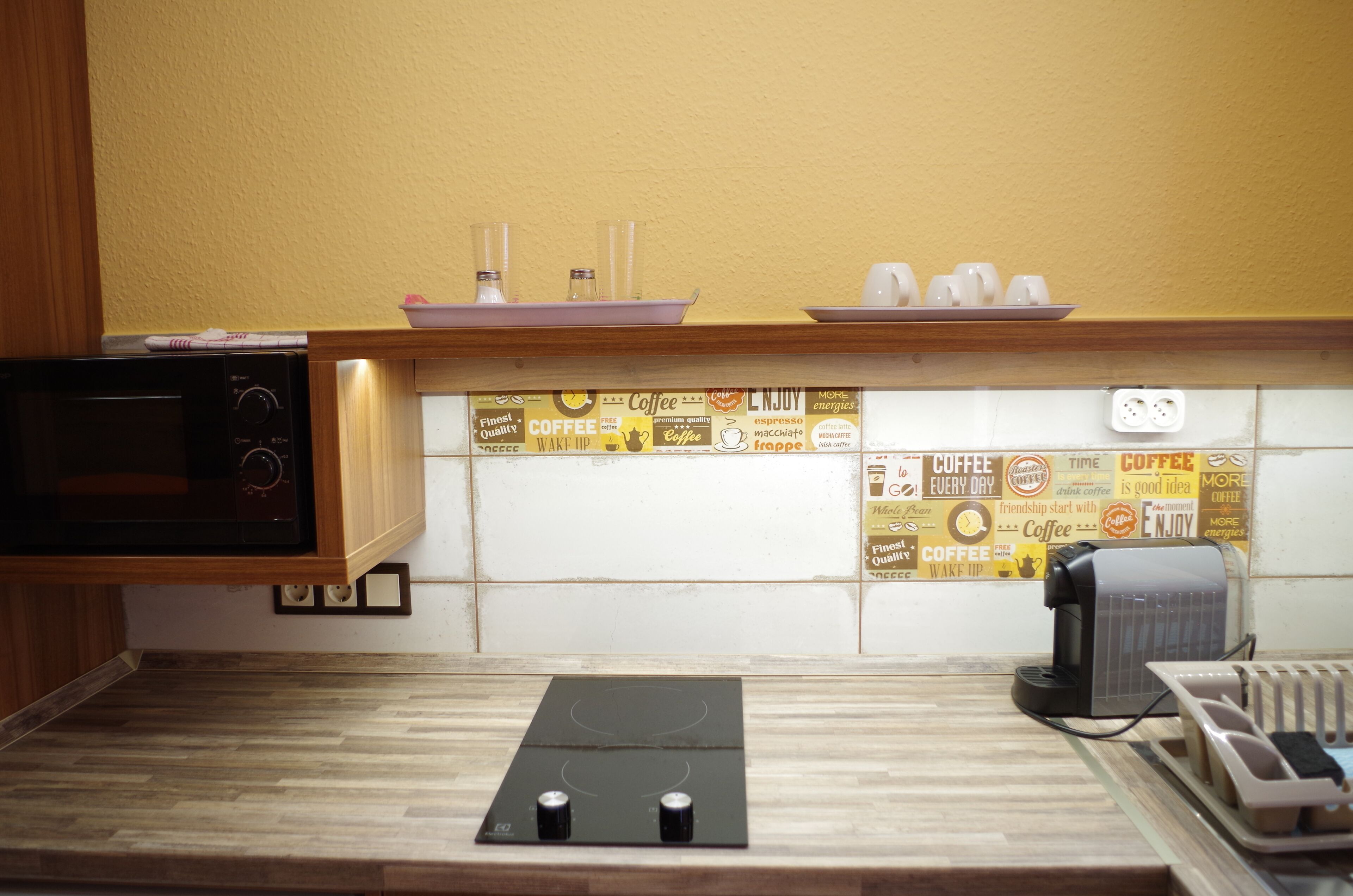 Una cocina equipada con microondas, cafetera y una zona de café con tazas y bandeja.