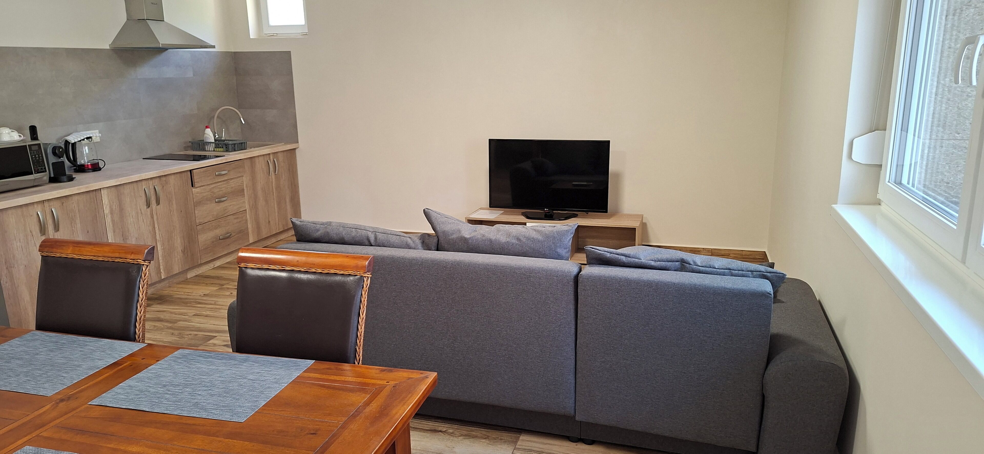 Un espacio habitable moderno con sofá, televisor, mesa de comedor y zona de cocina.