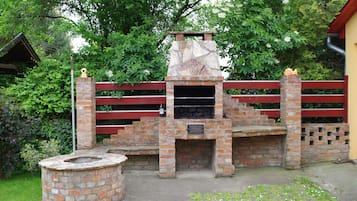 A brick-built outdoor barbecue area with a stone chimney, surrounded by a red fence and lush greenery.