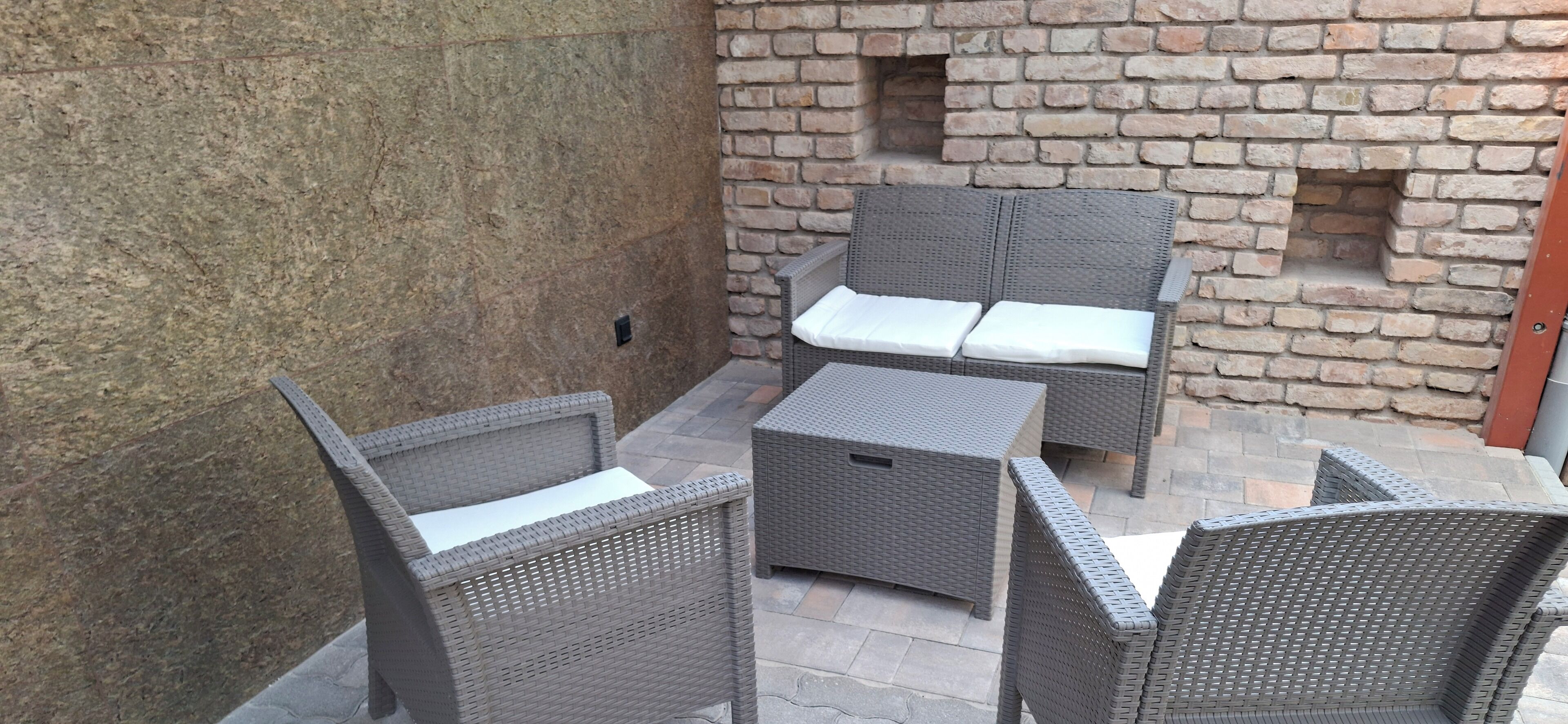 A patio area with wicker furniture and a brick wall.