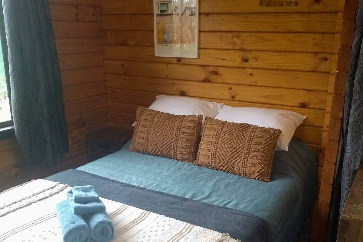 Une chambre dans un chalet en bois, avec un lit, deux oreillers, une couverture et des serviettes enroulées.