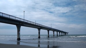 Une longue jetée s’étendant au-dessus de la plage, dotée d’une rambarde et soutenue par de nombreux piliers.
