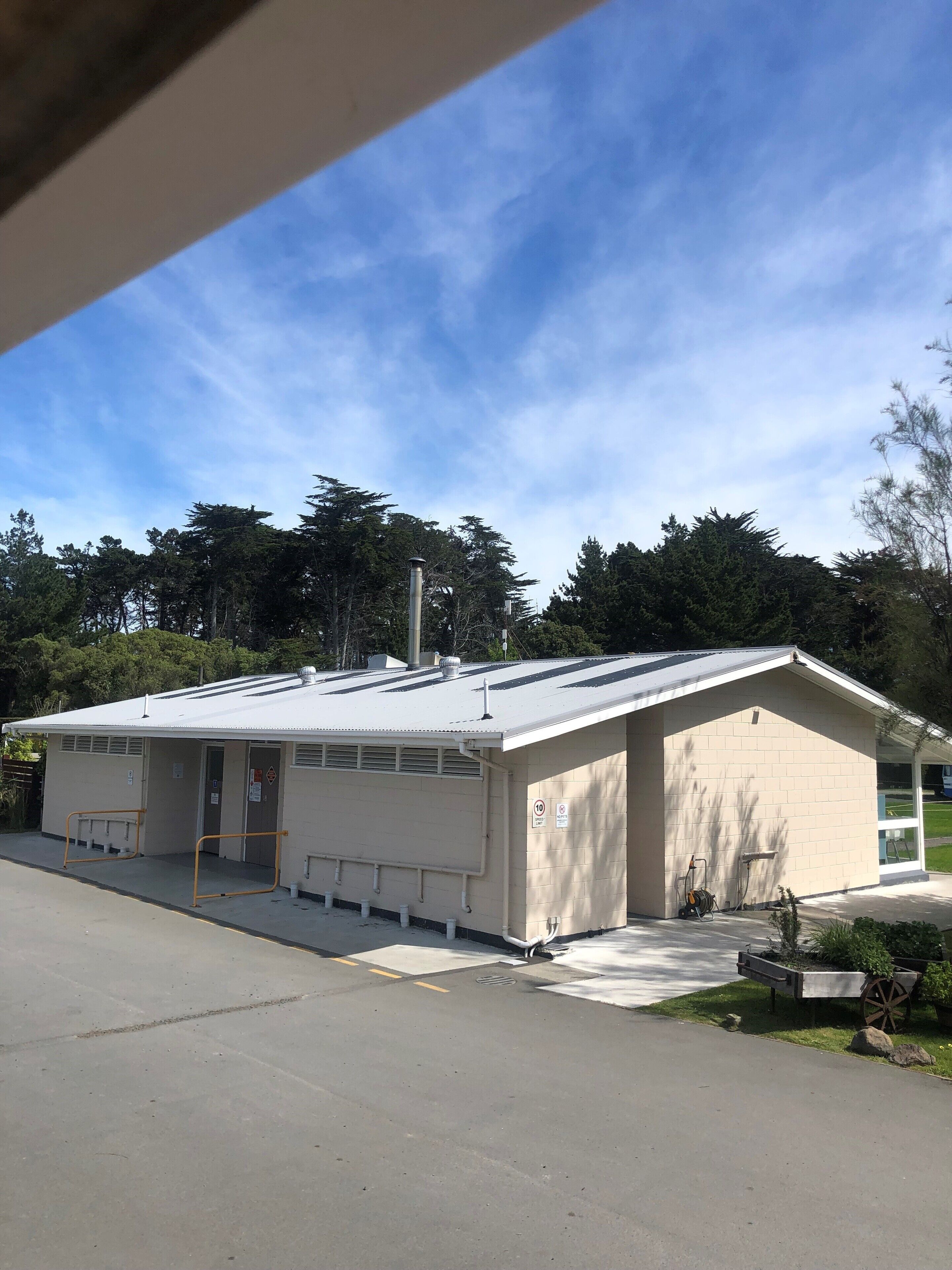 A small, single-story building with a flat roof, a covered entrance, and a small outdoor area with a bench.