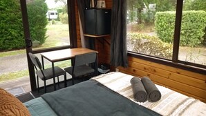Une pièce confortable avec un lit, un bureau et une chaise. Il y a une fenêtre avec des rideaux et un téléviseur posé sur une étagère.