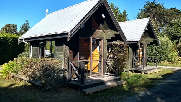 Une petite cabane avec un toit en pente, un revêtement extérieur en bois et une véranda dotée d’une balustrade.