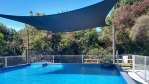 Une piscine aux eaux d’un bleu limpide, dotée d’un espace ombragé et entourée d’une clôture en métal et d’arbres.