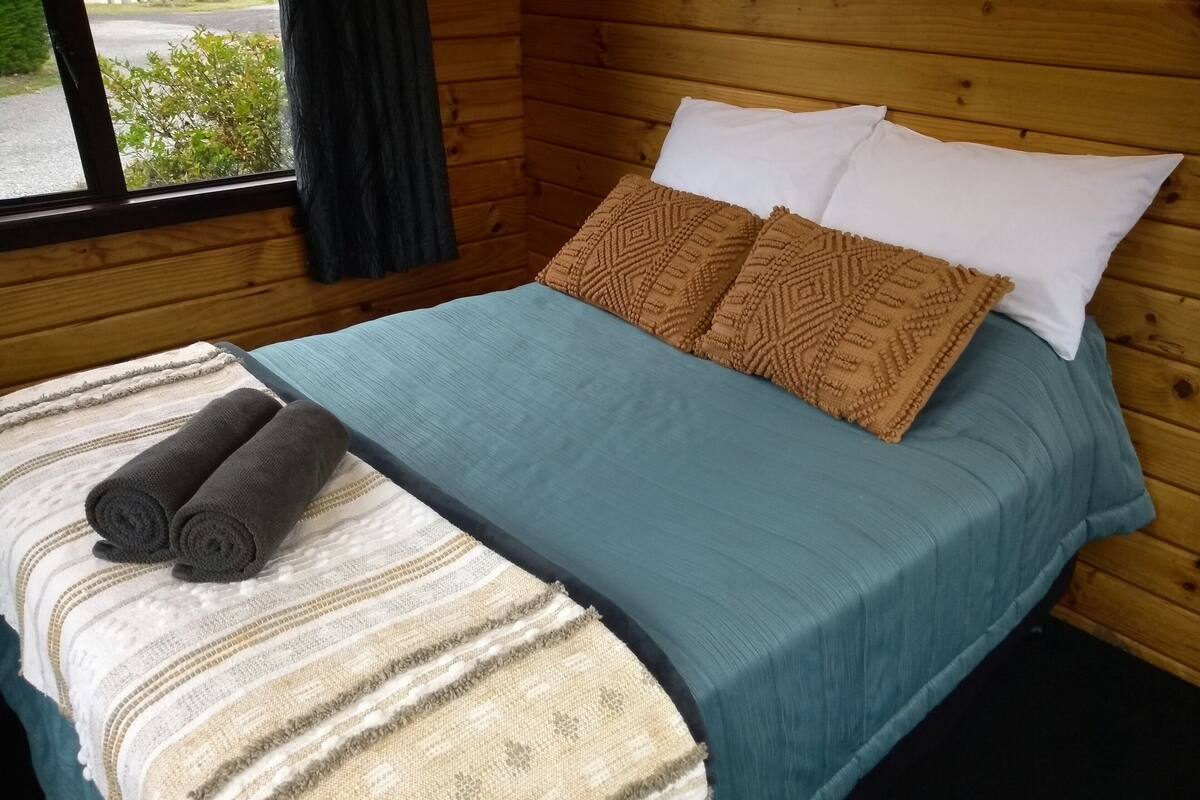 Une chambre dans un chalet en bois, avec un lit, des oreillers et une couverture.