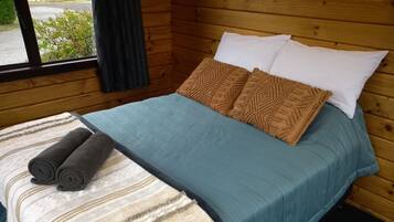 A wooden cabin room with a bed, pillows, and a blanket.