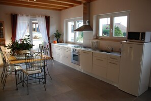 A modern kitchen with a dining area, featuring a large window, a microwave, and a refrigerator. - New Kertzfeld cottage, luxury performance in Alsace countryside. (Kertzfeld)