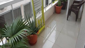 Ein Balkon mit Blumentöpfen, einem Metallgitter und einem Tisch mit einem Stuhl.