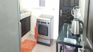 Eine kleine Küche mit Kühlschrank, Backofen und einer Kaffeemaschine auf einem Glastisch.