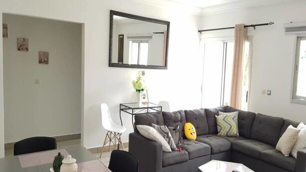 Ein modernes Wohnzimmer mit einem grauen Ecksofa, einem Esstisch mit Stühlen, einem Couchtisch und einem großen Spiegel an der Wand.