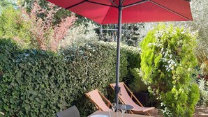 An outdoor dining area with a table set for four, surrounded by chairs, under a red umbrella. - Town house ideal for a couple with children (Arcachon)
