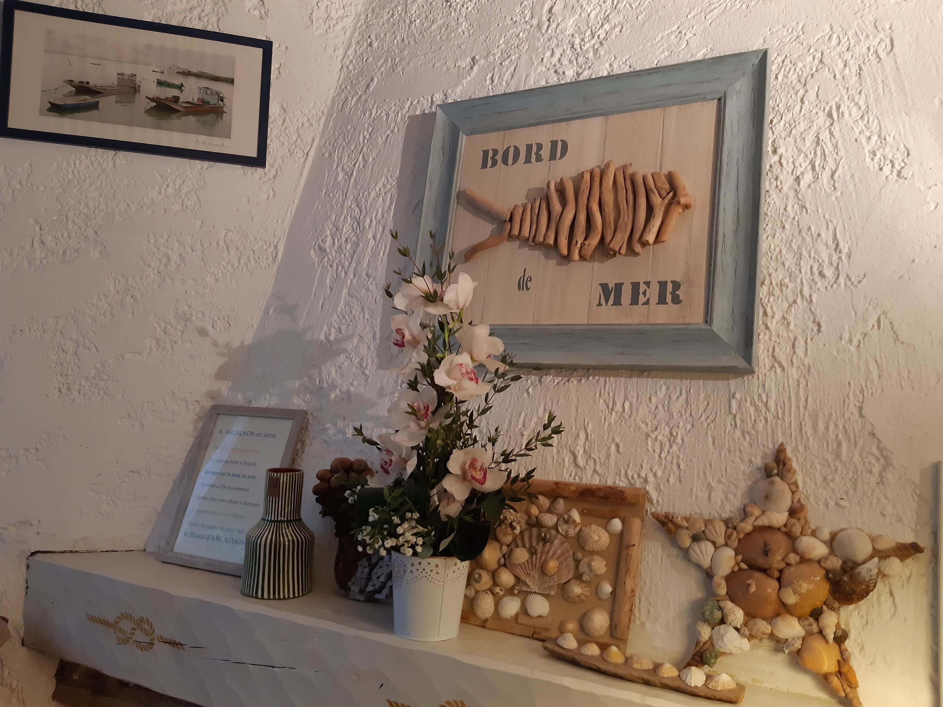A wall with a framed fish illustration, a small vase with flowers, and a shelf with decorative items.