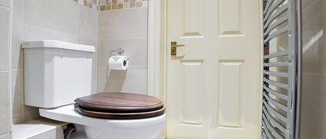 Un baño con inodoro, repisa de vidrio, toallero y puerta.