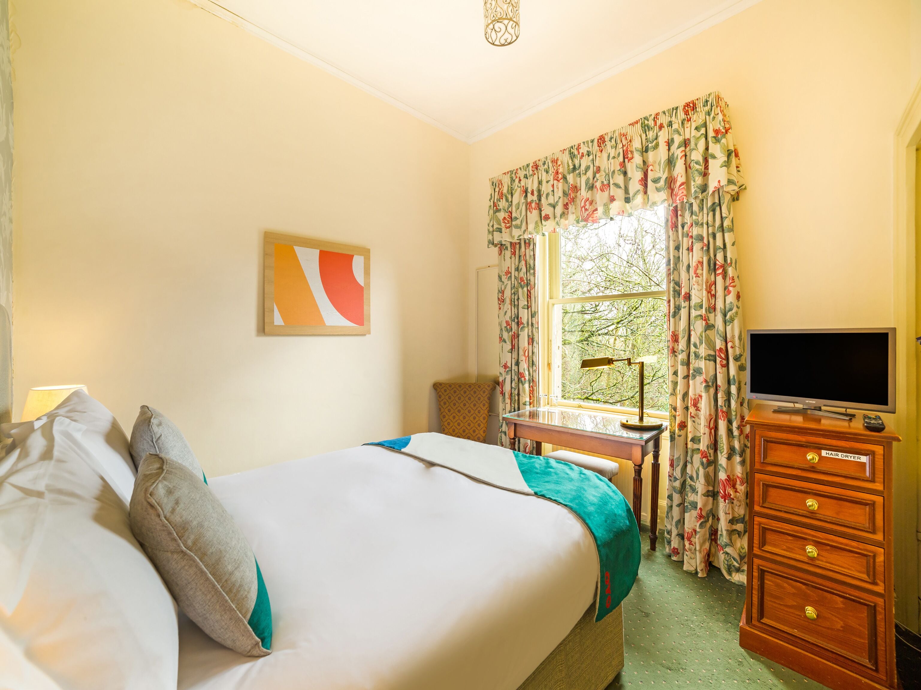 Una habitación de hotel con una cama, un escritorio, un televisor y un aparador.