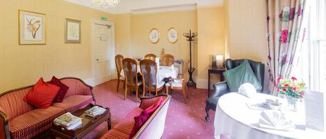 A hotel room with a dining area, a sofa set, a chandelier, and a table with a menu.