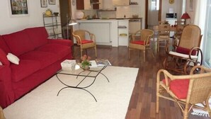 A compact living space with a red sofa, wicker chairs, a glass coffee table, and a kitchenette in the background. - CENTRE HISTORIQUE MAUSSANE, house 72 m2 with fenced garden,  (Maussane les alpilles)