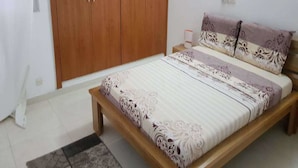 A bedroom with a wooden bed frame, a patterned bedspread, a nightstand, and a wardrobe. - Residence Cécilia (Abidjan)