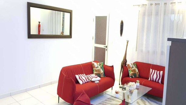 A living room with two red sofas, a glass coffee table, and a small rug. - Residence Cécilia (Abidjan)