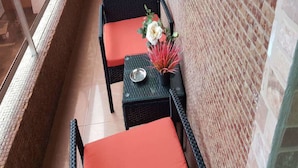 A narrow outdoor seating area with wicker furniture and orange cushions, a small table with a flower arrangement, and a brick wall. - Residence Cécilia (Abidjan)