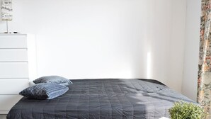 A minimalist bedroom with a bed, a dresser, and a potted plant.