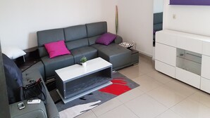A modern living room with a grey sofa, a white coffee table, and a red rug. - Résidence Esther 2 (Abidjan)