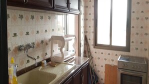 A kitchen with dark wooden cabinets, a sink, a window, and a stove. - Résidence Esther 2 (Abidjan)