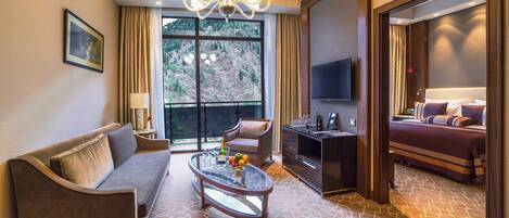 Una habitación de hotel con sofá, sillón, mesa de centro, televisor y cama.