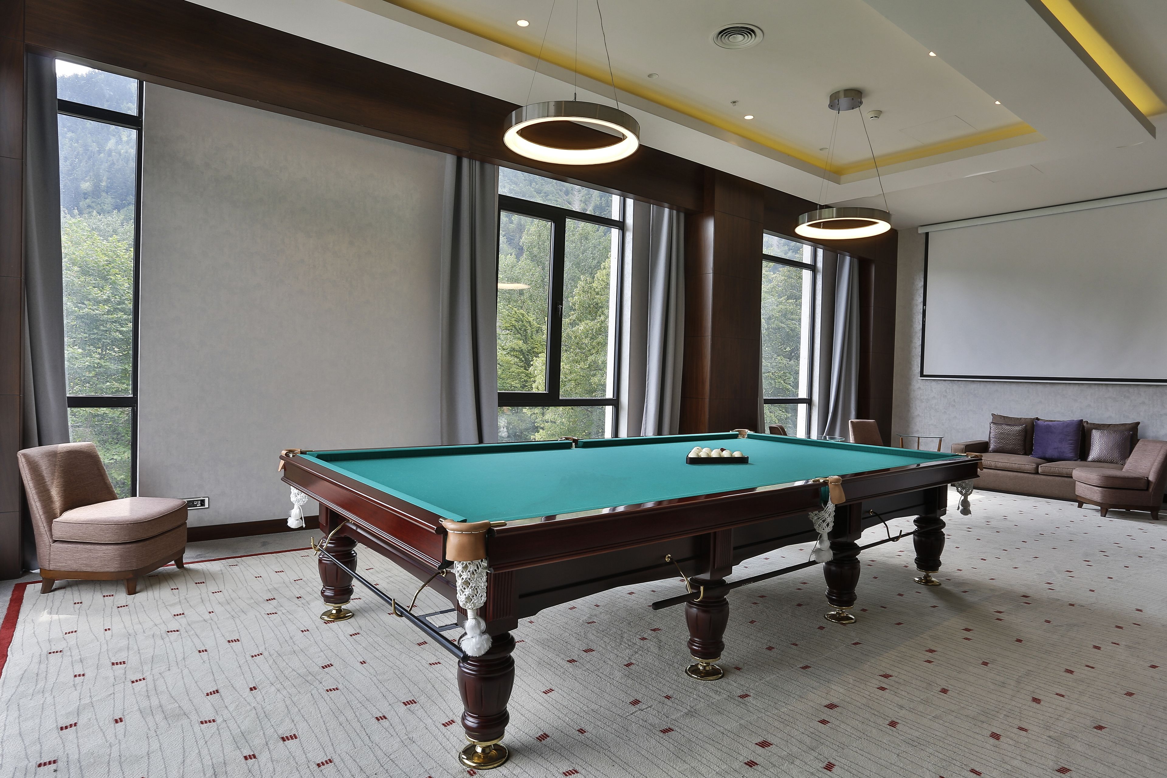 Una mesa de billar con superficie de fieltro verde, una vara de billar y una silla.