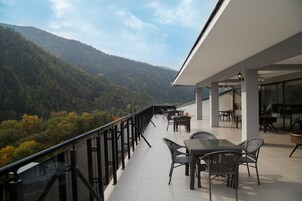 A balcony with a glass railing overlooking a forested valley.