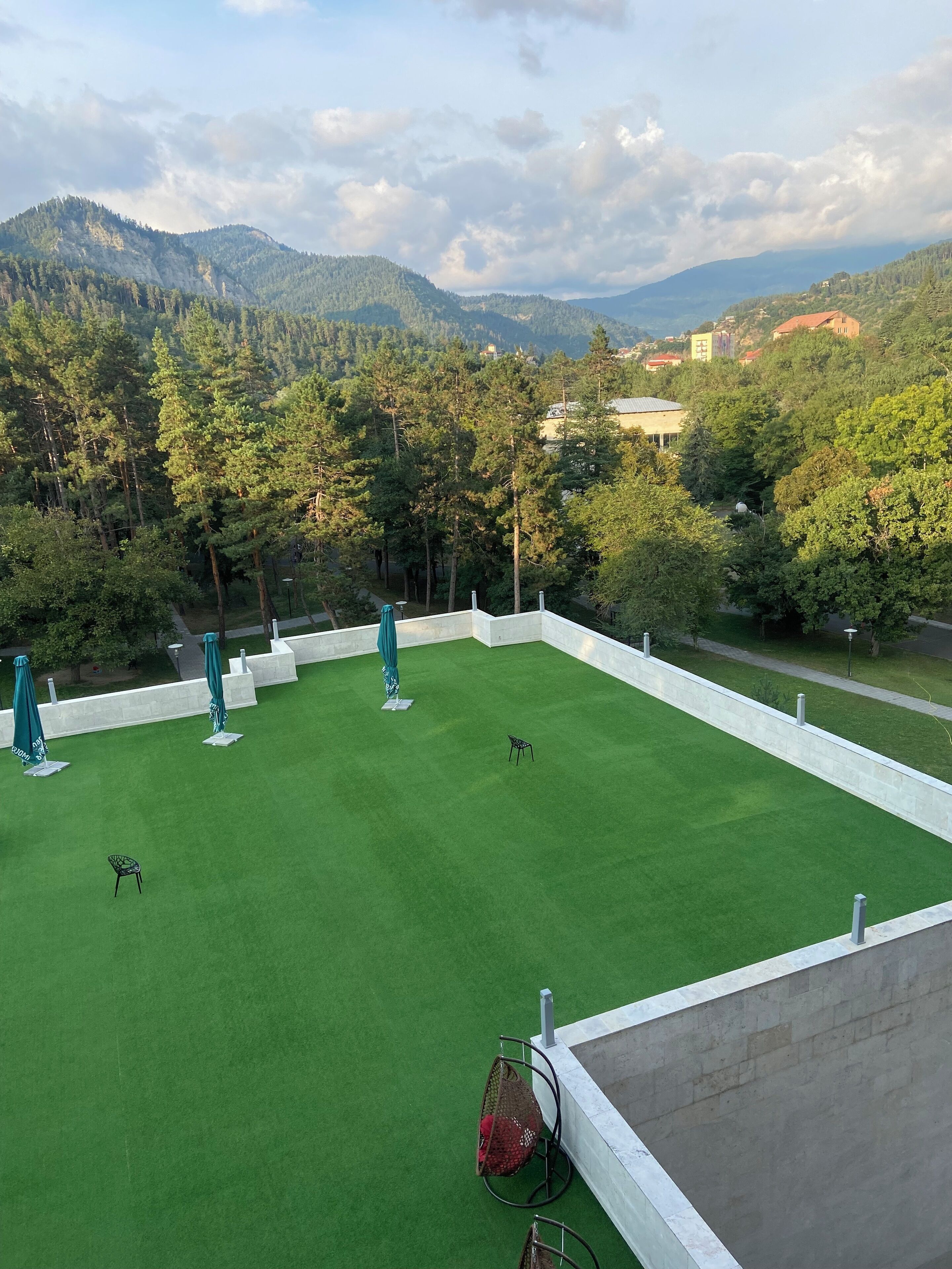 A rooftop terrace with artificial grass, outdoor seating, and a view of a forested mountain range.
