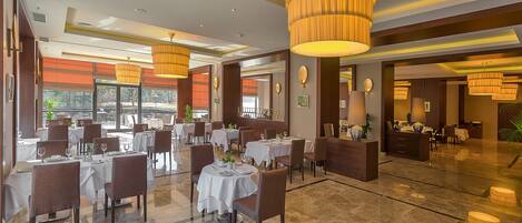A spacious restaurant with multiple dining tables, elegant chandeliers, and a modern interior design.
