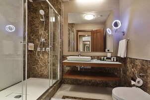 Un baño moderno con ducha acristalada, tocador de madera y un espejo grande con iluminación integrada.