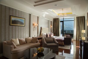 Habitación de hotel con una cama grande, un sofá, una mesita de centro con fruta y vistas al exterior.