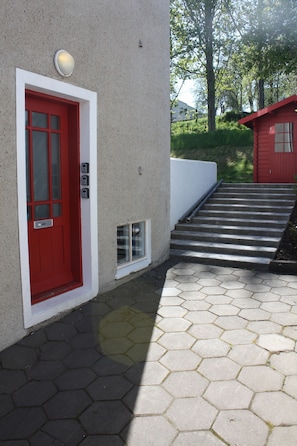 Una porta rossa con un'apertura piccola, un muro bianco e una scalinata che conduce a un edificio rosso.