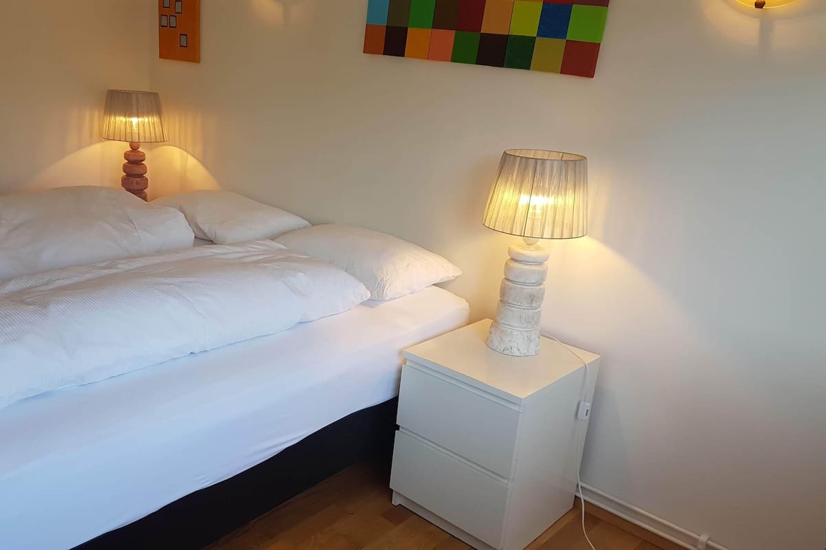A neatly made bed with white linens and two bedside lamps.