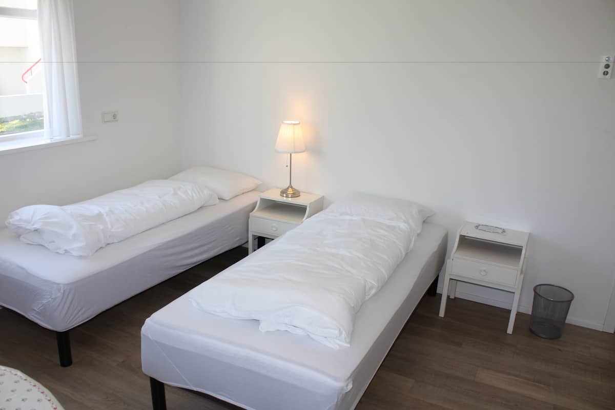A twin room with two single beds, a bedside table with a lamp, a small shelf, and a waste bin.