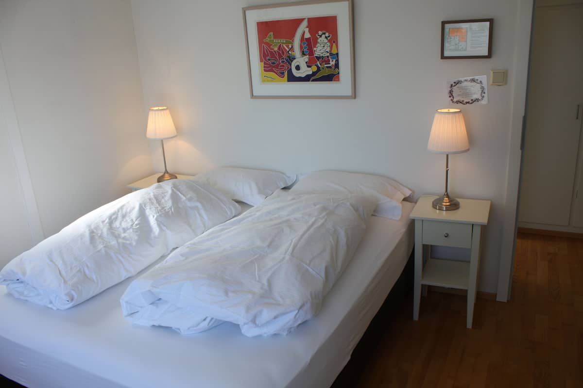 A neatly made bed with white linens, two bedside lamps, and a framed artwork above the bed.