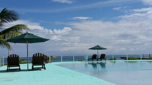 Ein Poolbereich mit Liegestühlen und Sonnenschirmen, mit Blick auf den Ozean und einem gefliesten Deck.