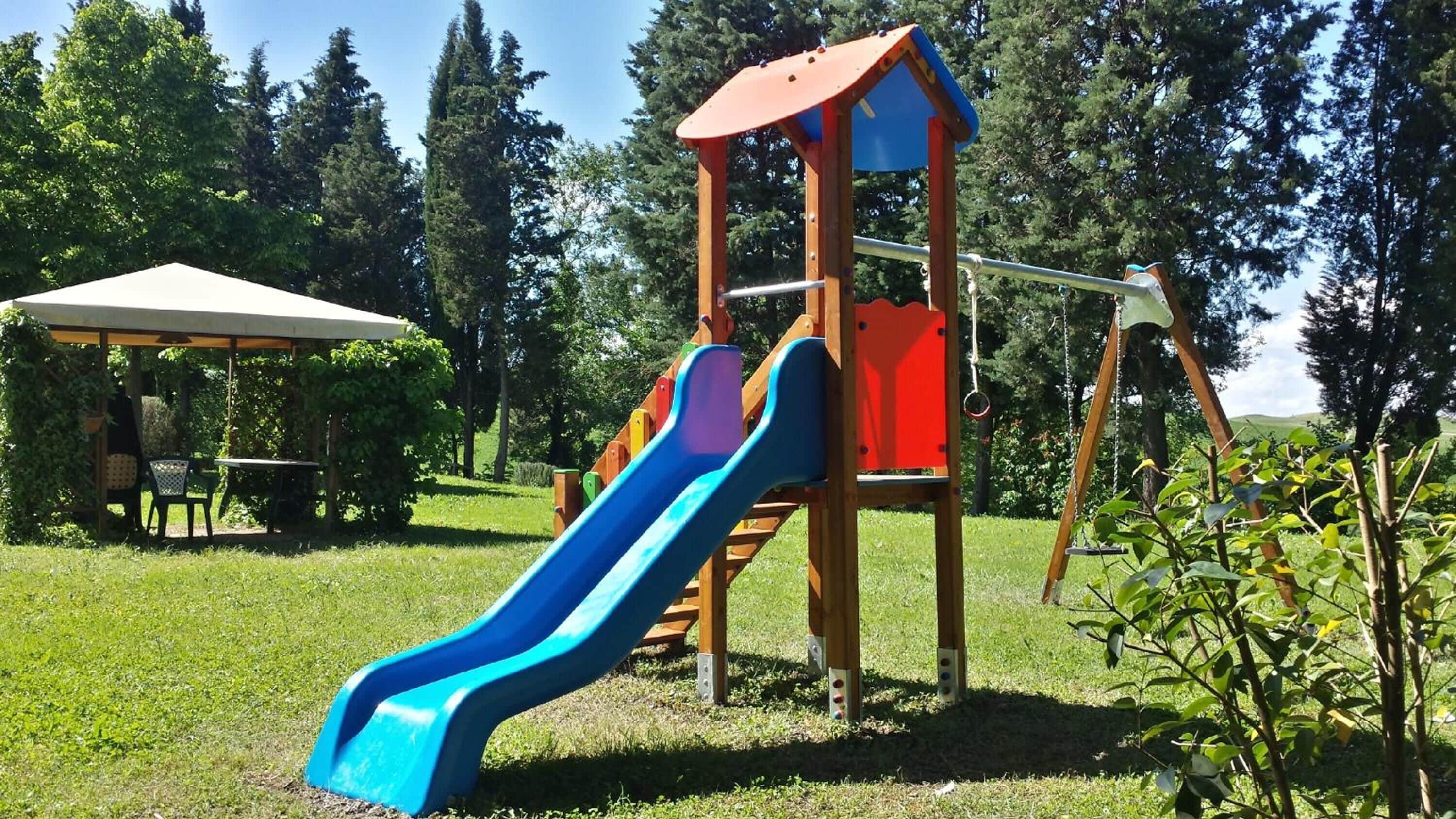 Un parque infantil con un tobogán azul, una estructura roja para escalar y un área de picnic con mesa y sillas.