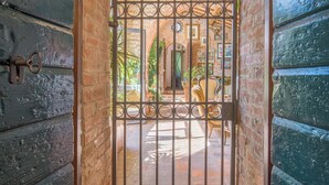 Un ingresso rustico con cancello in metallo, muri in mattoni e arco in pietra che conduce a un cortile.