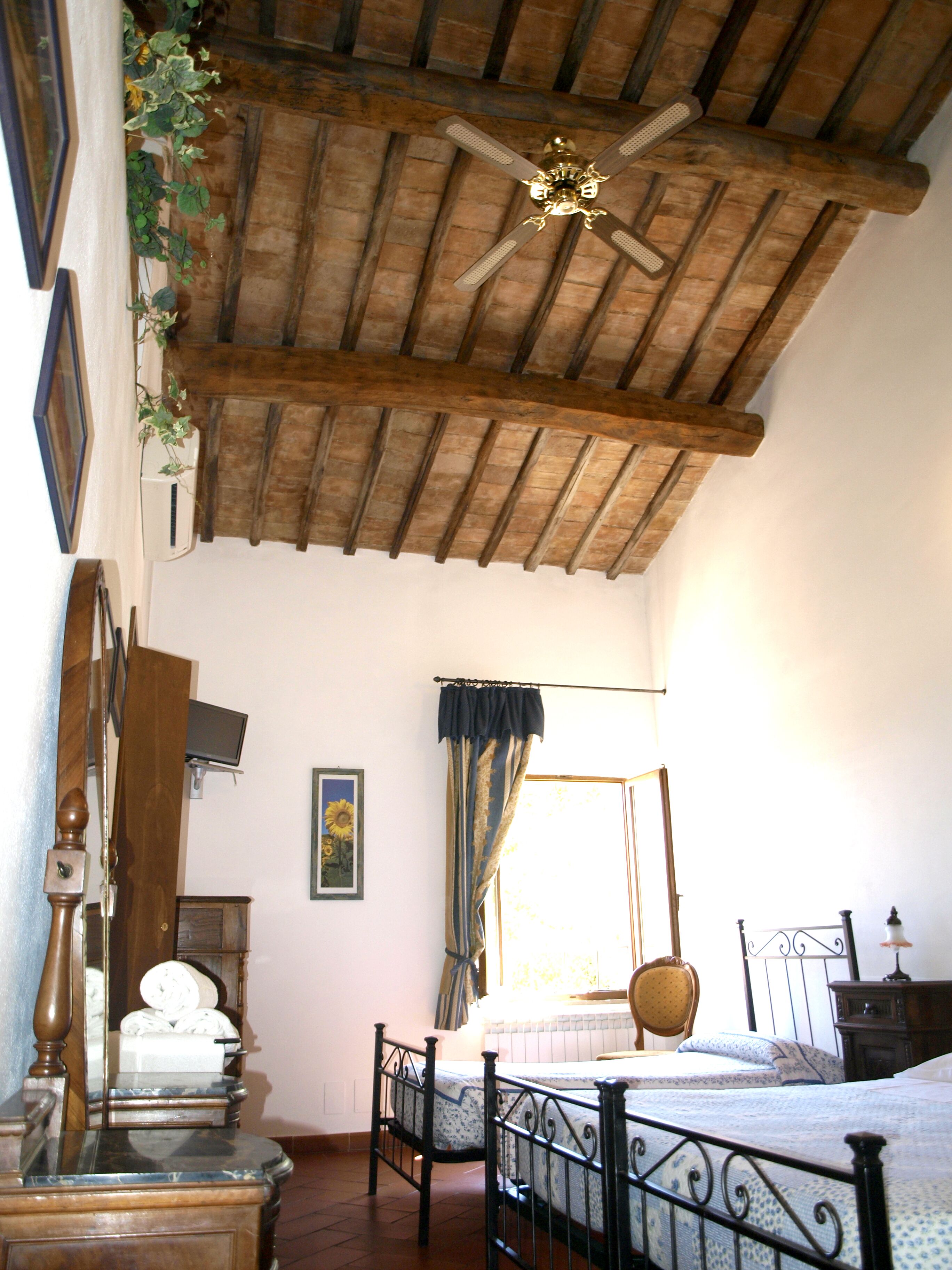 Een slaapkamer met houten plafond, een bed, een stoel, een nachtkastje en een raam met gordijnen.