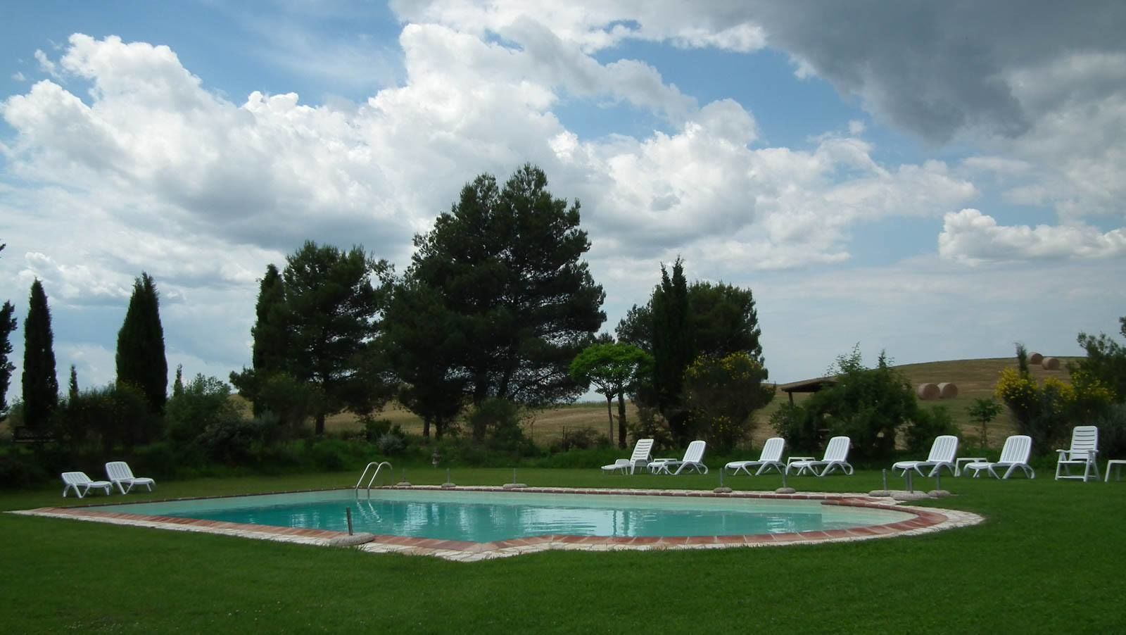 Una piscina con lettini prendisole, circondata da alberi e da un prato.
