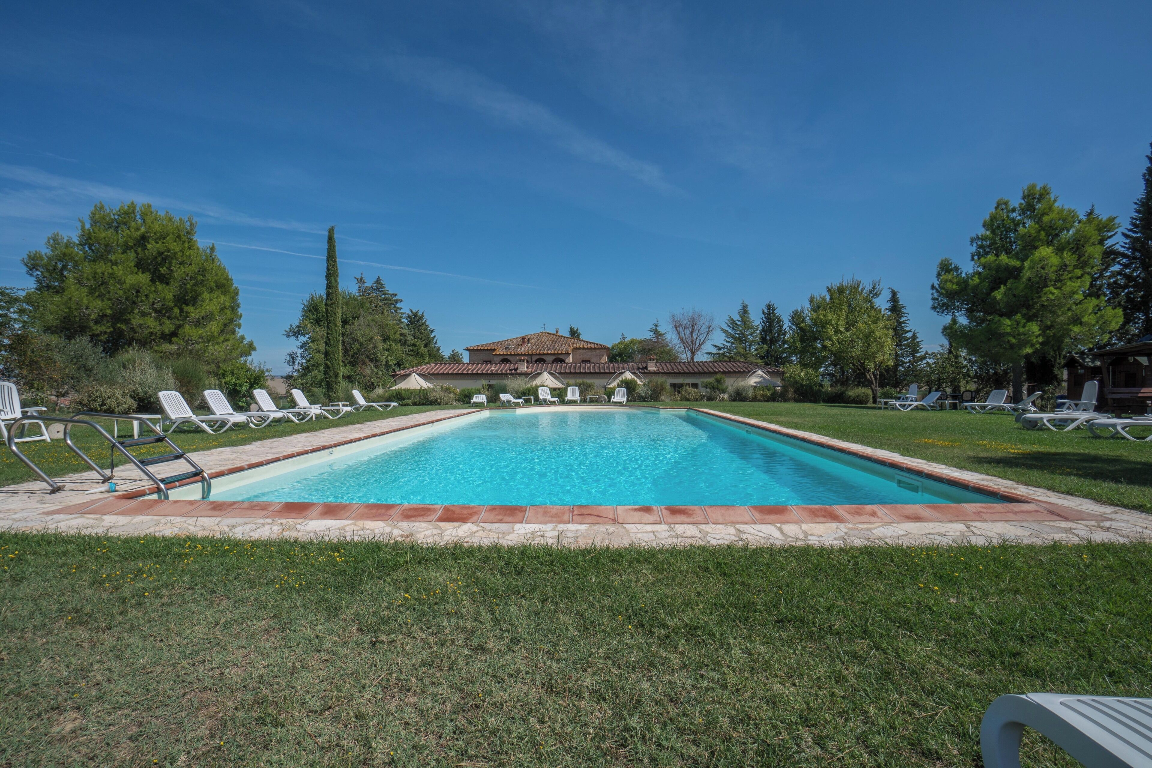 A rectangular swimming pool with a tiled edge, surrounded by a grassy area with white lounge chairs.